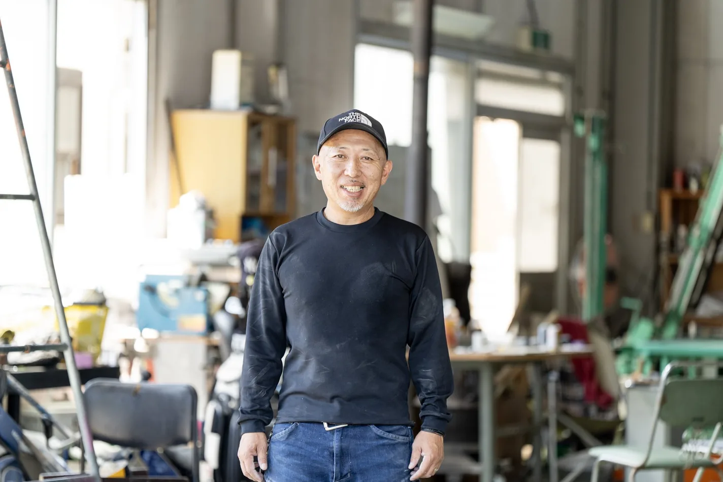 代表・3代目 倉林俊之が作業場で笑顔で立つ人物カット